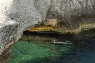 A girl swims under a stone bridge by the white rocks on the coast at Sarakinikoer, Milos, Cyclades,
