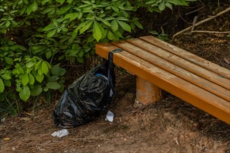 A black trash bag left beside a wooden bench in nature, in South Korea