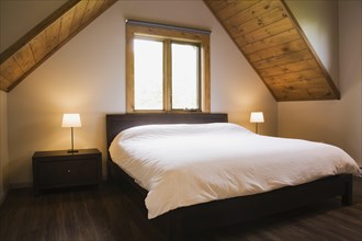 King size bed in master bedroom on upstairs floor inside contemporary style log home, Quebec,