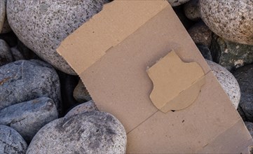 A plain cardboard shape surrounded by stones, hinting at environmental disregard, in South Korea
