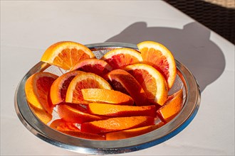 A glass bowl full of fresh orange slices in the sunlight