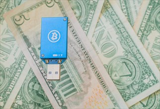 A blue USB hardware wallet with a Bitcoin logo on a background of US dollar bills, in South Korea