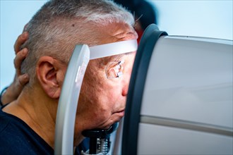 Side view close-up of a senior man leaning the head on scanner to check glaucoma