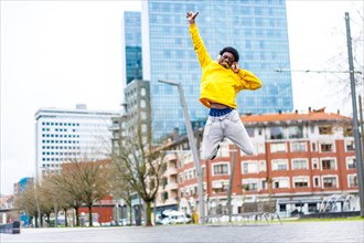 Full length photo of a young African cool man jumping happily while listening to music in the city