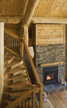 High angle view of wooden and black wrought iron staircase and lit natural stone fireplace in