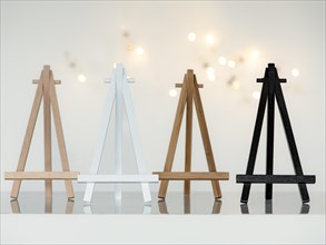 Four small wooden mini easels in the colours beech, white, bamboo and black, standing next to each