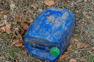 Weathered blue plastic barrel with a green cap surrounded by leaves, in South Korea