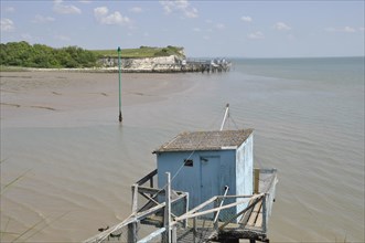 Wooden hut and walkway on a tranquil beach with low tide under a clear blue sky, fishery in Talmon