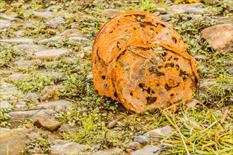 A rusty, decayed bucket lies on a grassy cobblestone surface, showing signs of erosion, in South
