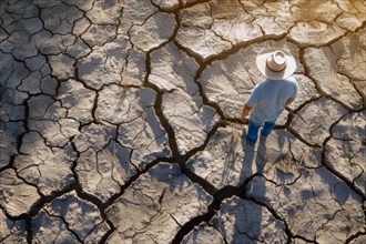 A farmer stands on a parched, cracked earth surface, due to lack of water, drought, extreme