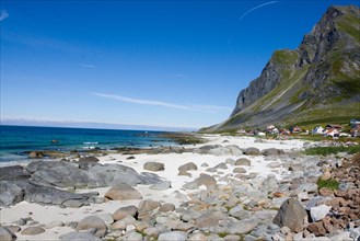 An idyllic sandy beach with rocks and clear water against a backdrop of mountains and blue skies