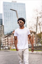 Vertical photo of a cool and casual stylish african man wearing sunglasses walking along a city