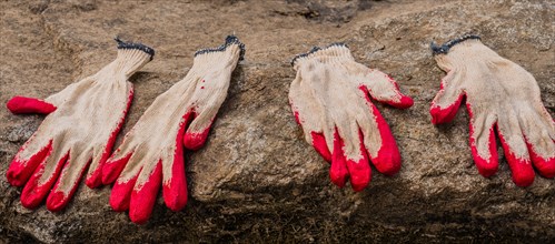 Two pairs of red and cream work gloves left on a muddy surface, in South Korea