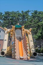 An inflatable slide with a dragon design at a playground surrounded by trees, in Ulsan, South