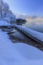 Morning atmosphere at mountain lake in front of mountains, boat huts, shore, winter, snow,