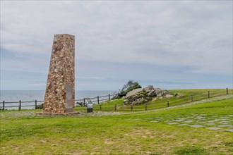 Stone monument in a grassy field with ocean in the background and cloudy skies, in Ulsan, South