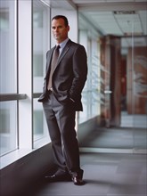 Businessman in suit and tie standing thoughtfully by a window in a modern office environment, AI