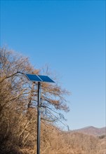 Small solar panel on top of chrome pole in front of leafless trees against blue sky in Buan, South