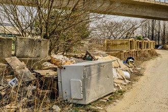 Discarded appliances and debris outside with a man scavenging nearby, in South Korea