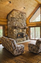 Upholstered sofas with lit fieldstone and porous rock fireplace in living room inside handcrafted