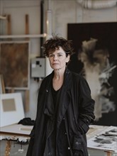 An artist stands contemplatively in her studio, surrounded by pieces of art, AI generated