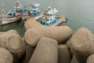 Fishing boats docked at a marina, surrounded by concrete wave blocks on a cloudy day, in Ulsan,