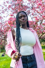 Vertical portrait of a young african woman in casual clothes posing next to flowering pink tree
