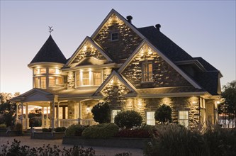 Elegant grey stone with white trim and blue asphalt shingles roof Victorian home facade at dusk in