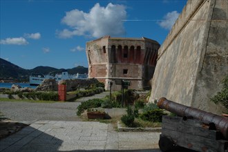 Old fortress with cannon in the foreground and a ship on the sea in the background Elba Island