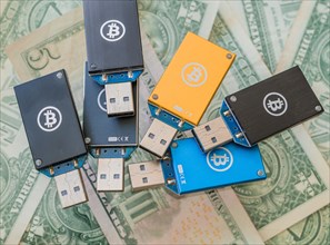 Various USB hardware wallets with Bitcoin logos on them, displayed on US dollar bills, in South