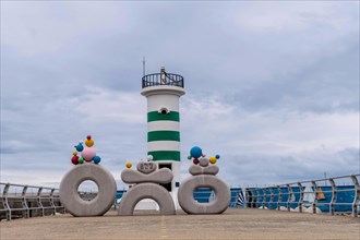A playful striped lighthouse adorned with balloons on a pier beside the ocean, in Ulsan, South