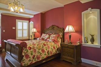 Wooden sleigh bed and night table in master bedroom on upstairs floor inside elegant style home,