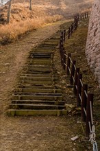 Wooden stairs on mountainside beside section of mountain fortress wall made of flat stones located