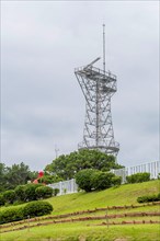 Tall metal radar tower standing amidst lush greenery under a cloudy sky, in Ulsan, South Korea,