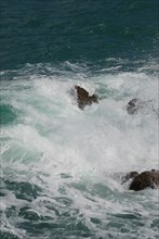 Turbulent waves crash against rocks, creating sea foam in the aquamarine ocean
