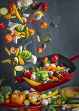 Colourful vegetables are thrown up from a pan while cooking, dark background