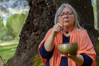 Mature woman with white hair meditating in the forest with her eyes closed and a Tibetan singing