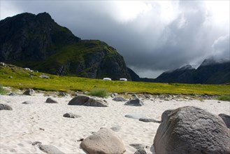 View of a dramatic mountain landscape with meadow, stones and a cloudy sky Lofoten