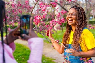African young female friends taking photos next to a cherry tree in spring