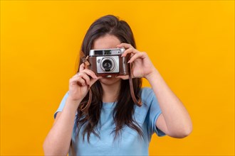 Studio portrait with yellow background of a casual young woman using a old fashioned camera