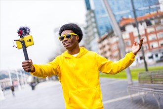 Cool african young content creator with yellow clothes streaming online in the city using mobile