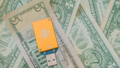 An orange USB hardware wallet with a Bitcoin logo lying on US dollar bills, in South Korea