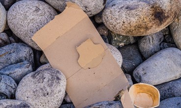 Discarded piece of cardboard lying among gray stones, symbolizing pollution, in South Korea