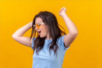 Studio portrait with yellow background of a happy woman wearing sunglasses dancing and celebrating