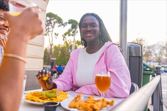 Smiling african young woman eating nachos with friends in an outdoor restaurant