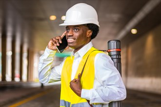 Side view close-up portrait of a busy young african architect wearing protective gear talking to