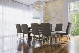 Glass dining table with gray upholstered high back chairs in dining room inside luxurious home,