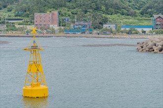 A yellow navigation buoy bobs in the ocean under a cloudy sky, marking safe passage, in Ulsan,