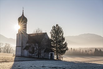 Chapel at sunrise in front of mountains, backlight, sunbeams, hoarfrost, winter, Sankt