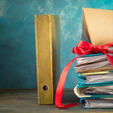 A golden folder next to a pile of papers, both wrapped with a red ribbon, symbolising bureaucracy,